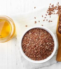 flaxseeds in a small serving bowl with a wooden spoon and a side of flaxseed oil