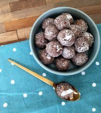 chocolate and almond meal protein balls covered with coconut flour served in a blue bowl with a blue and white polka dotted tea towel